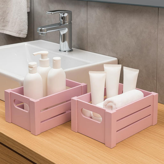WOOD CURLS set of two pink wooden storage crates with handles holding toiletries on a bathroom vanity counter.