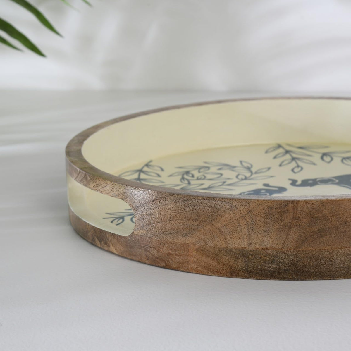 WOOD CURLS round wooden serving tray with cream base, blue elephant and leaf motifs, and cutout handles.