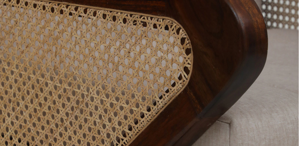 Close-up of WOOD CURLS Aarav sofa armrest featuring handwoven cane paneling and rich provincial teak Sheesham wood.