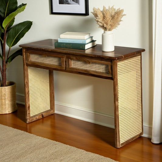 WOOD CURLS Aster console desk in natural acacia wood with woven cane drawer fronts and side panels in a home setting.