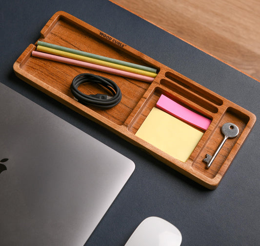 WOOD CURLS acacia wood desk organizer tray with stationery, a key, and charging cable on a dark office desk.