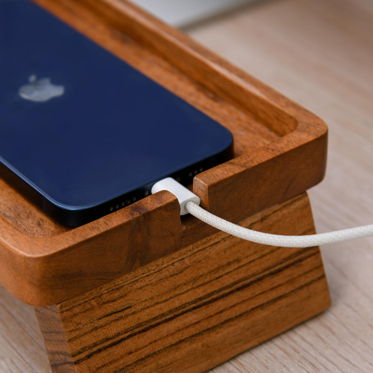 WOOD CURLS handcrafted acacia wood desk organizer holding a dark blue smartphone with a white charging cable attached.