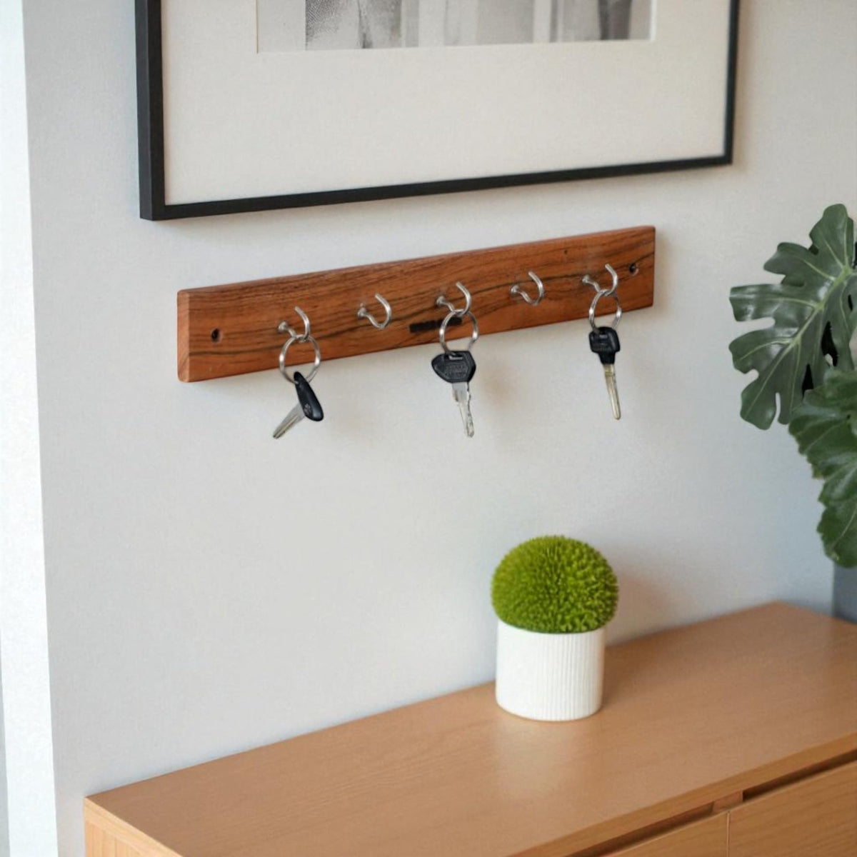 WOOD CURLS wall-mount key holder made of natural acacia wood with 5 metal hooks mounted on a white entryway wall.