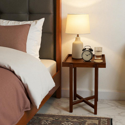 WOOD CURLS Enigma square acacia wood side table with a lamp, alarm clock, and glass of water in a bedroom setting.