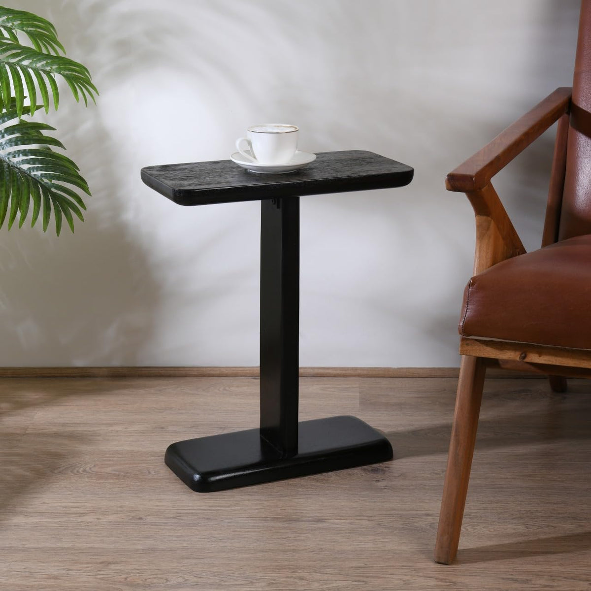 WOOD CURLS black mango wood C-frame side table with a coffee cup on top, placed next to a brown leather armchair.