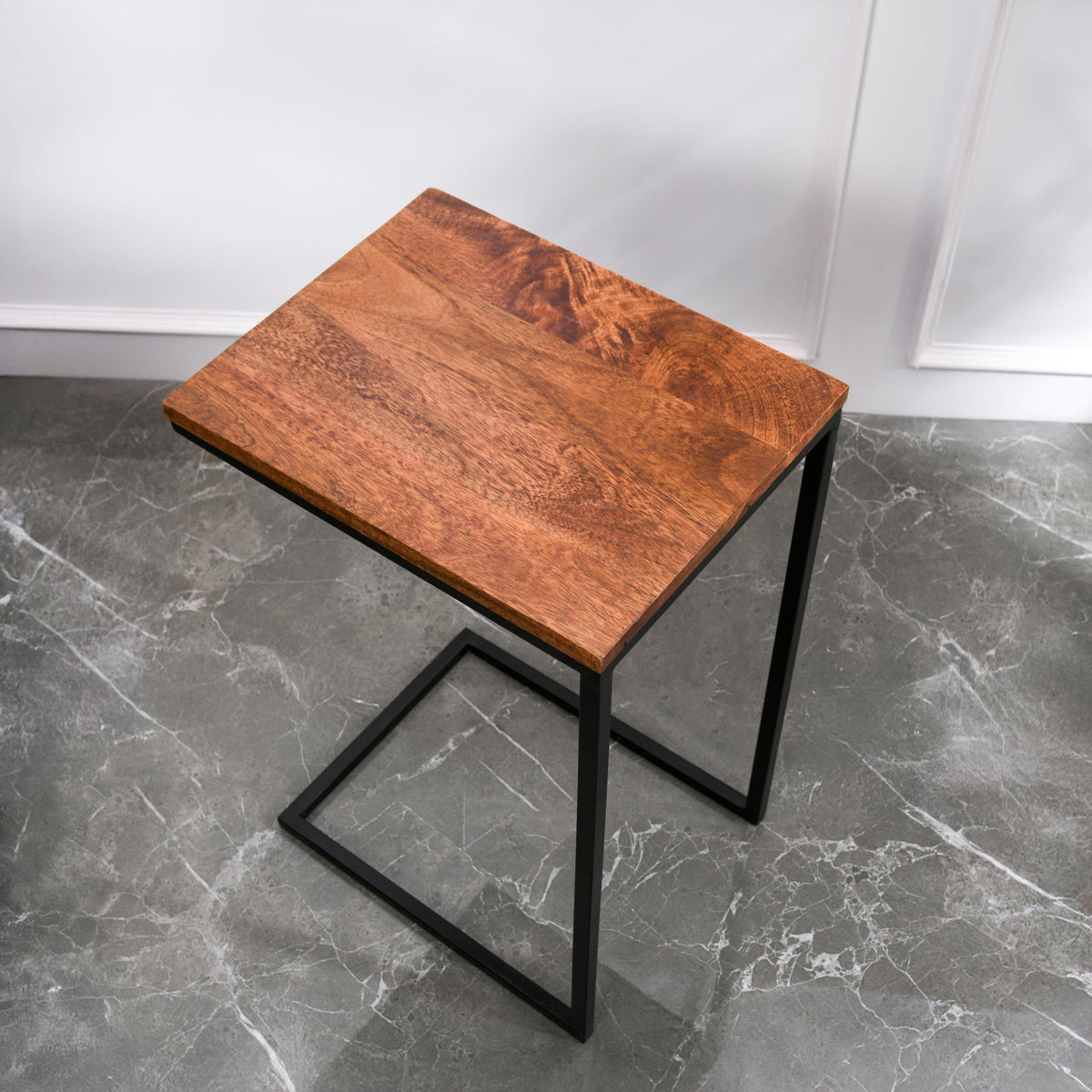 WOOD CURLS Odyssey C-shape side table with a warm mango wood top and a durable black iron frame on a marble floor.