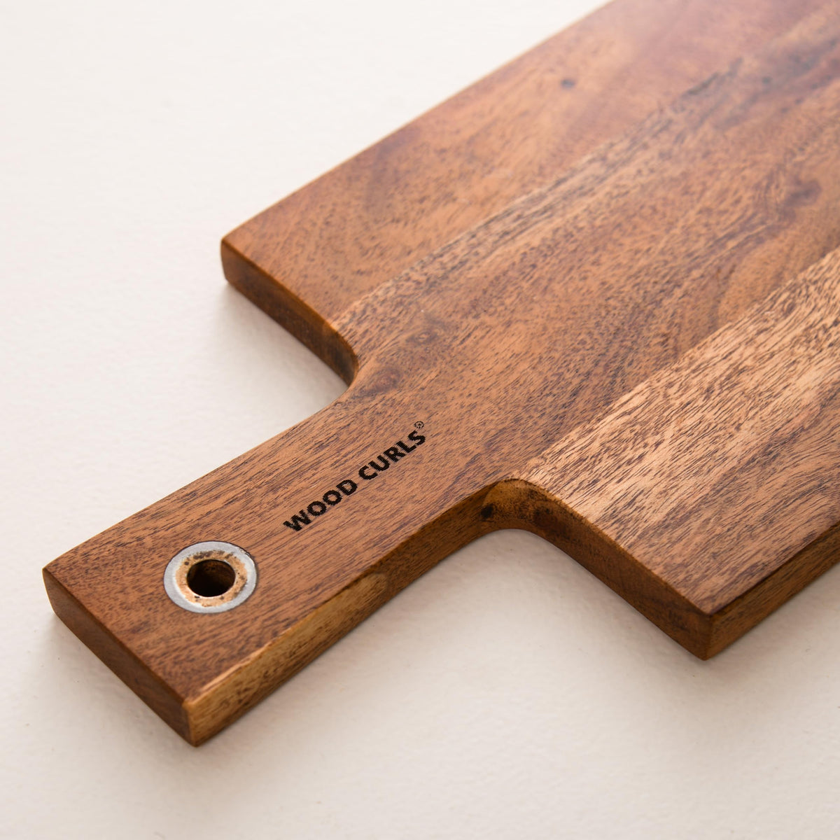 WOOD CURLS long acacia wood charcuterie board with a handle and metal hanging loop on a white background.