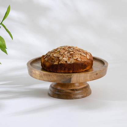 WOOD CURLS 23 cm round mango wood pedestal cake stand holding a small almond cake on a white surface