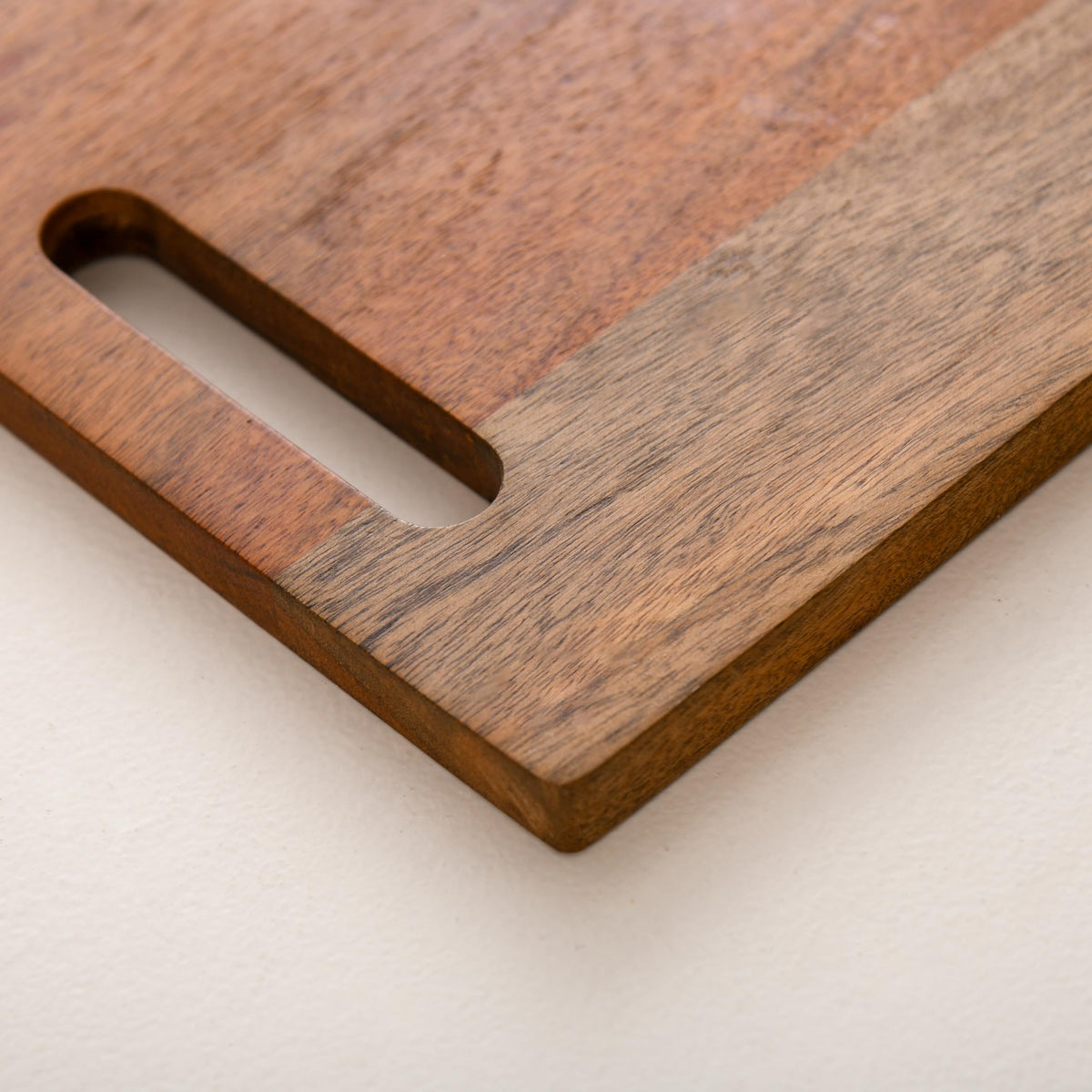 WOOD CURLS rectangular mango wood chopping board with a built-in handle and natural wood grain finish.