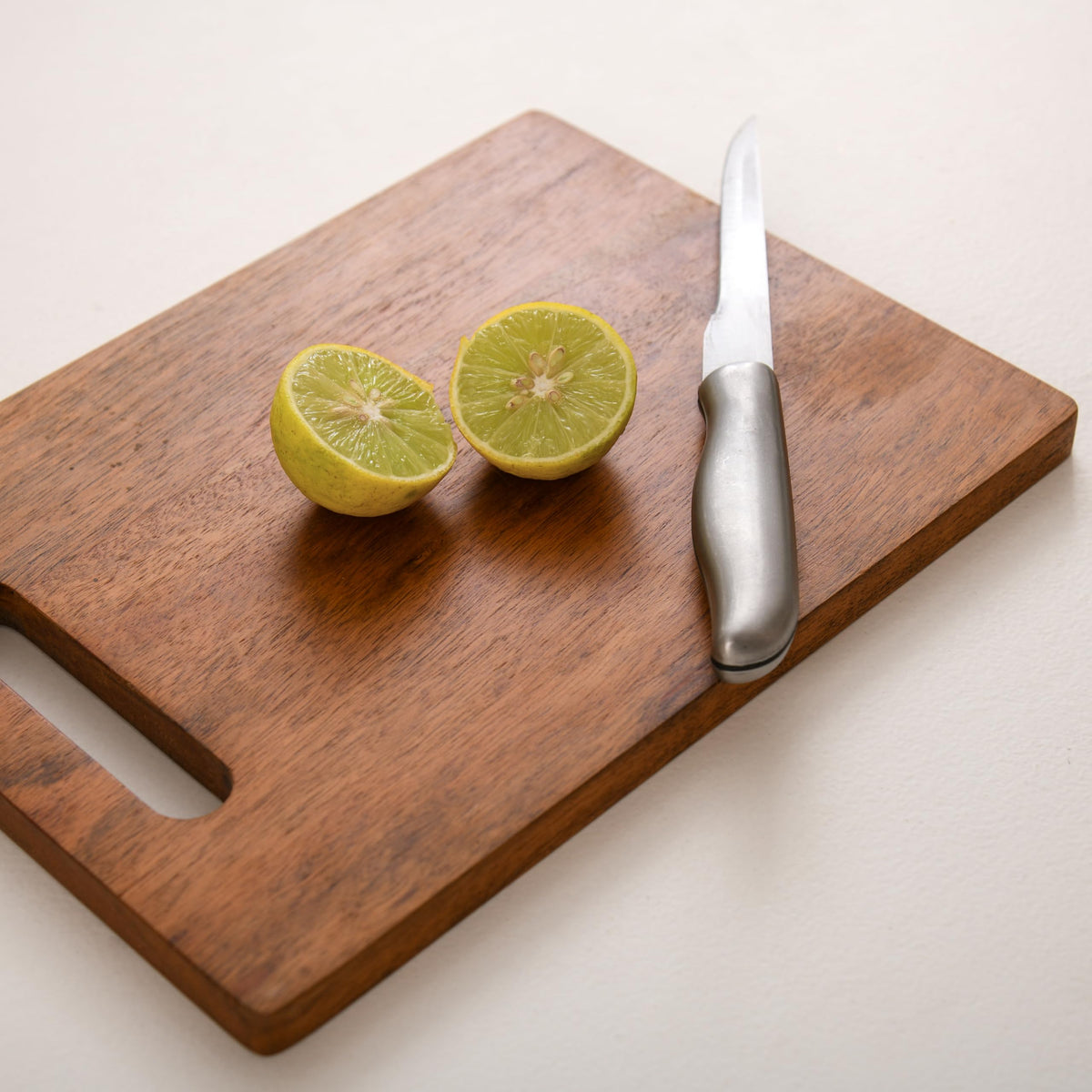 WOOD CURLS rectangular mango wood chopping board with a metal knife and sliced lime on a white surface.
