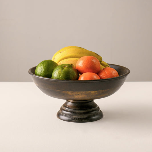 WOOD CURLS mango wood pedestal bowl with a walnut finish, filled with fresh fruit on a neutral background.