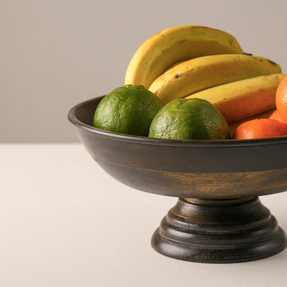 WOOD CURLS mango wood pedestal bowl with a walnut finish, filled with fresh fruit on a neutral table surface.