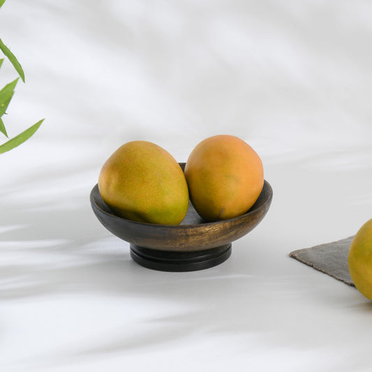WOOD CURLS small mango wood pedestal bowl in dark brown holding two fresh mangoes on a white surface