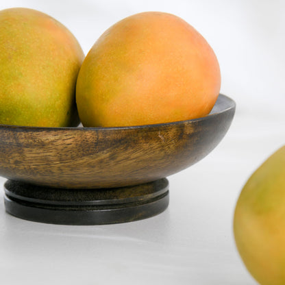 WOOD CURLS small mango wood pedestal bowl in dark brown finish holding fresh mangoes on a white surface