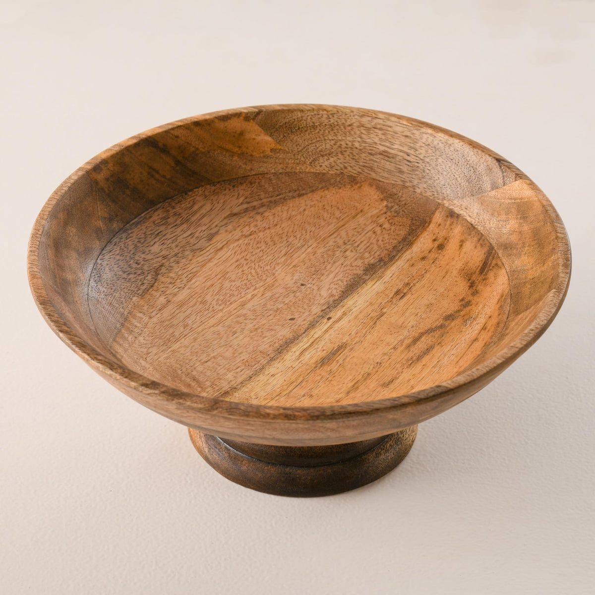 WOOD CURLS handcrafted mango wood pedestal bowl with a natural finish and visible wood grain patterns.