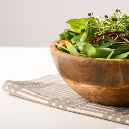WOOD CURLS 10-inch mango wood serving bowl filled with fresh green salad on a patterned grey napkin
