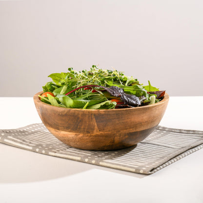 WOOD CURLS 10-inch mango wood serving bowl filled with fresh mixed salad greens on a grey patterned cloth napkin