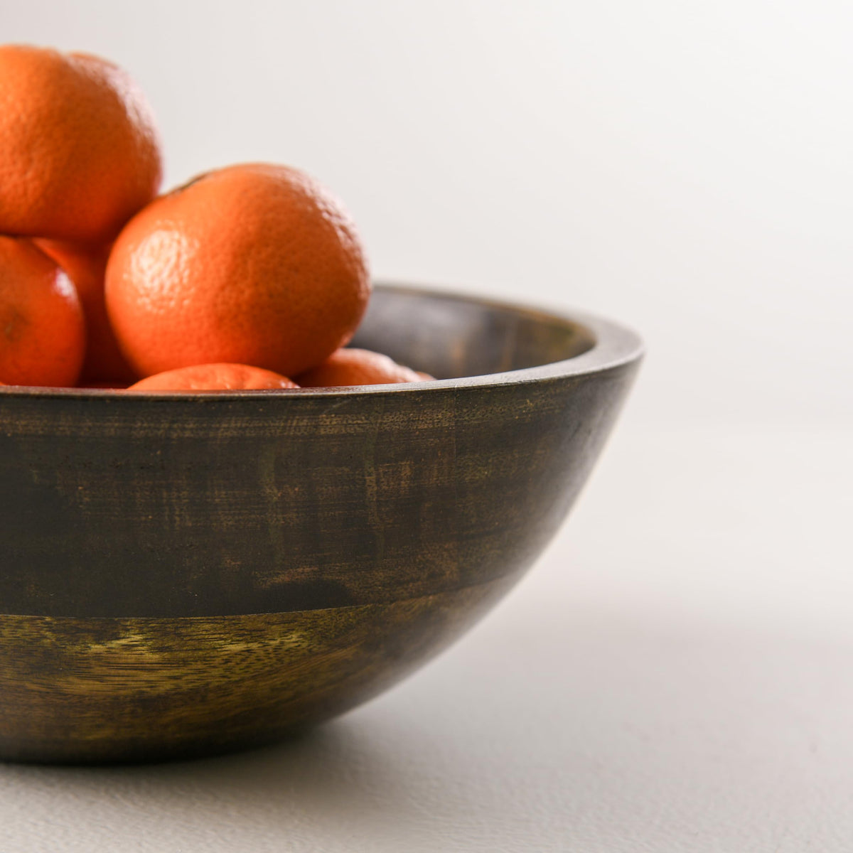 WOOD CURLS 10-inch round mango wood serving bowl with a walnut finish, filled with fresh oranges on a neutral surface.