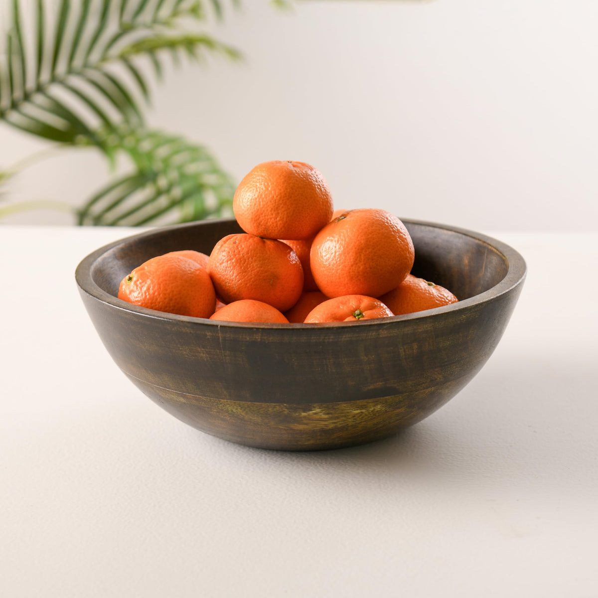WOOD CURLS 10-inch round mango wood serving bowl with a walnut finish filled with fresh oranges on a white table.