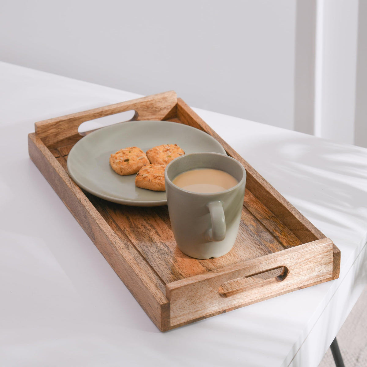 WOOD CURLS rectangular mango wood serving tray with handles holding a sage green plate of cookies and a coffee mug.