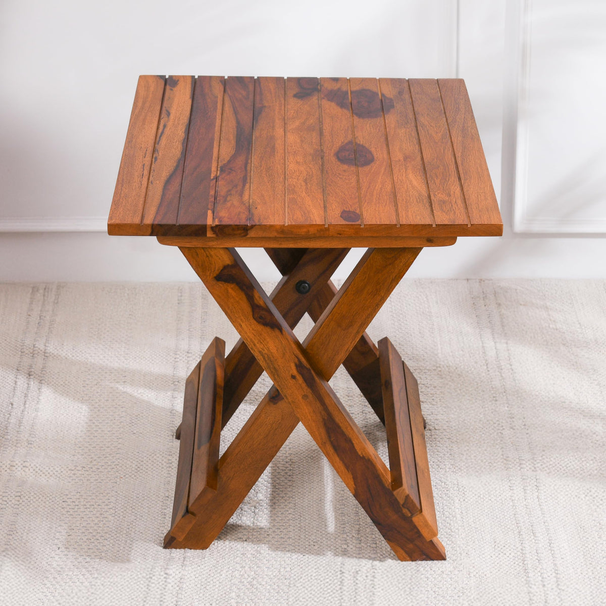 WOOD CURLS Nova square coffee table in natural Sheesham wood with a folding X-frame base on a textured rug.
