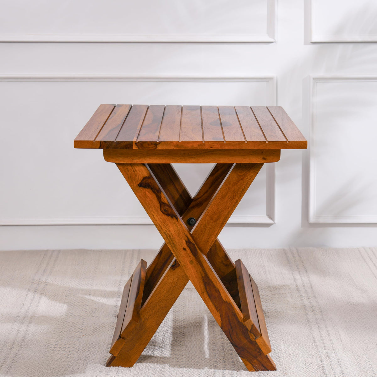 WOOD CURLS Nova square coffee table in natural Sheesham wood with a unique X-frame base against a white wall.