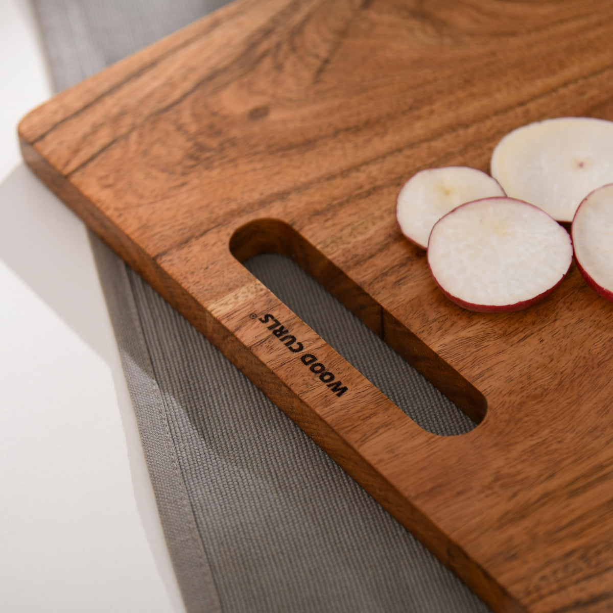 WOOD CURLS rectangular wooden chopping board with natural grain and handle, featuring sliced radishes on top.