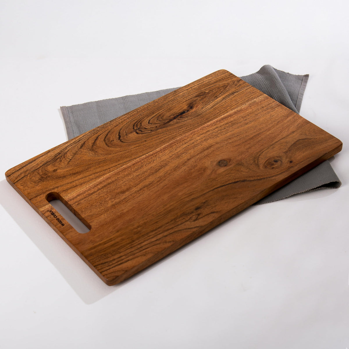 WOOD CURLS rectangular wooden chopping board with natural grain patterns and a built-in handle on a grey cloth