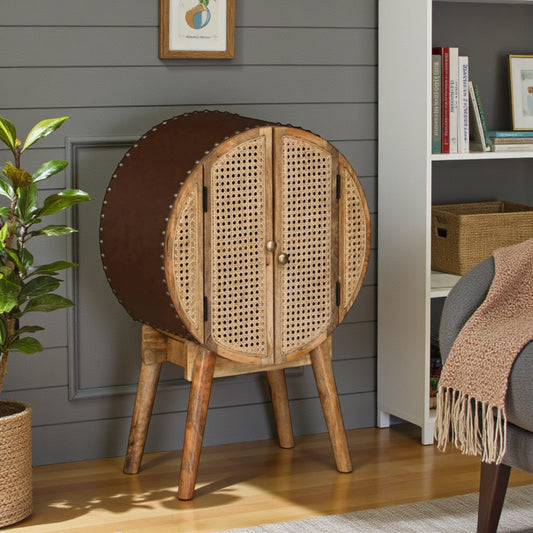 WOOD CURLS round mango wood cabinet with woven cane doors, leatherette back, and tapered legs in a living room.