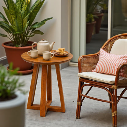 WOOD CURLS round mango wood coffee table with tea set and biscuits next to a rattan chair on a patio.