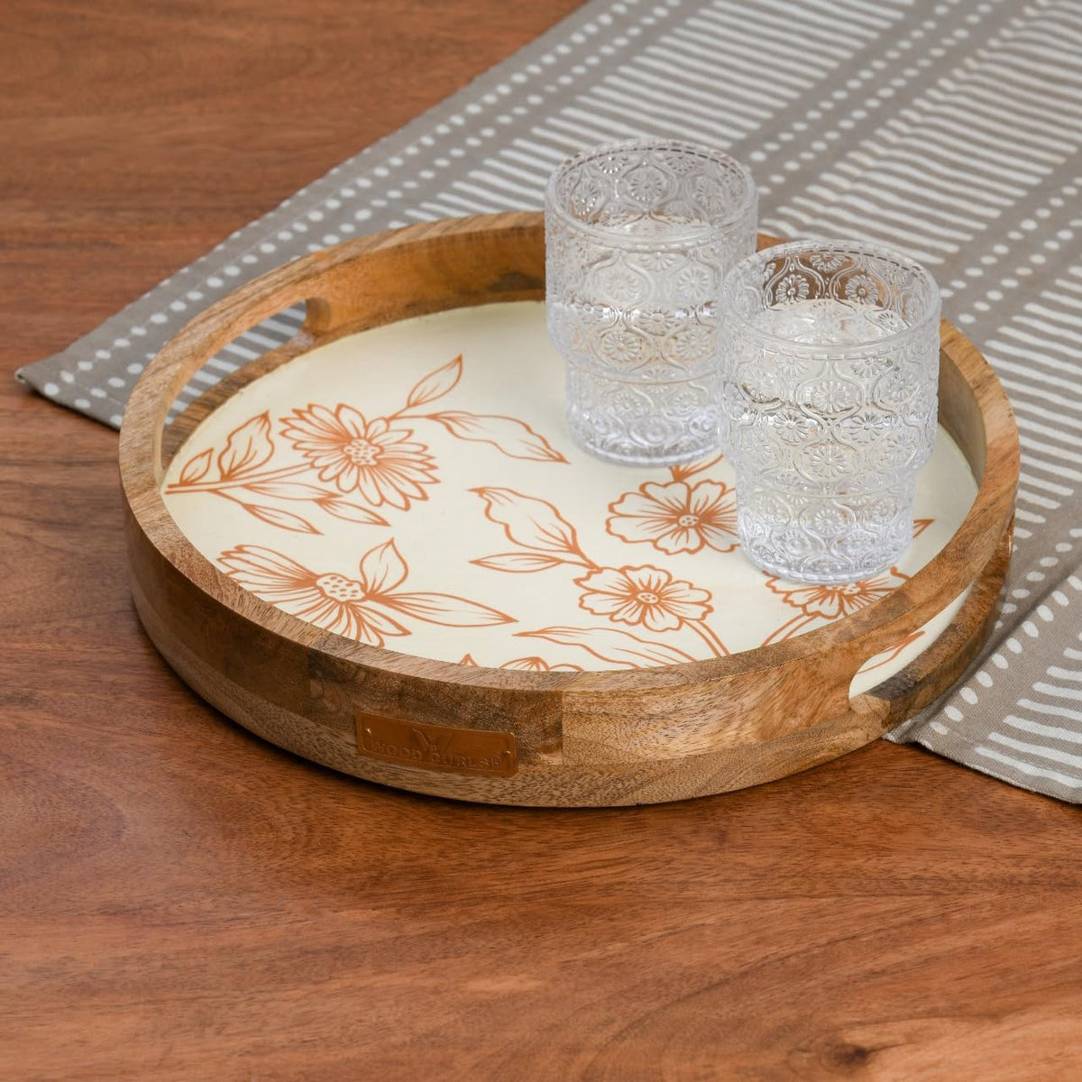 WOOD CURLS round mango wood serving tray with cream base and copper floral design, holding two textured glass tumblers.