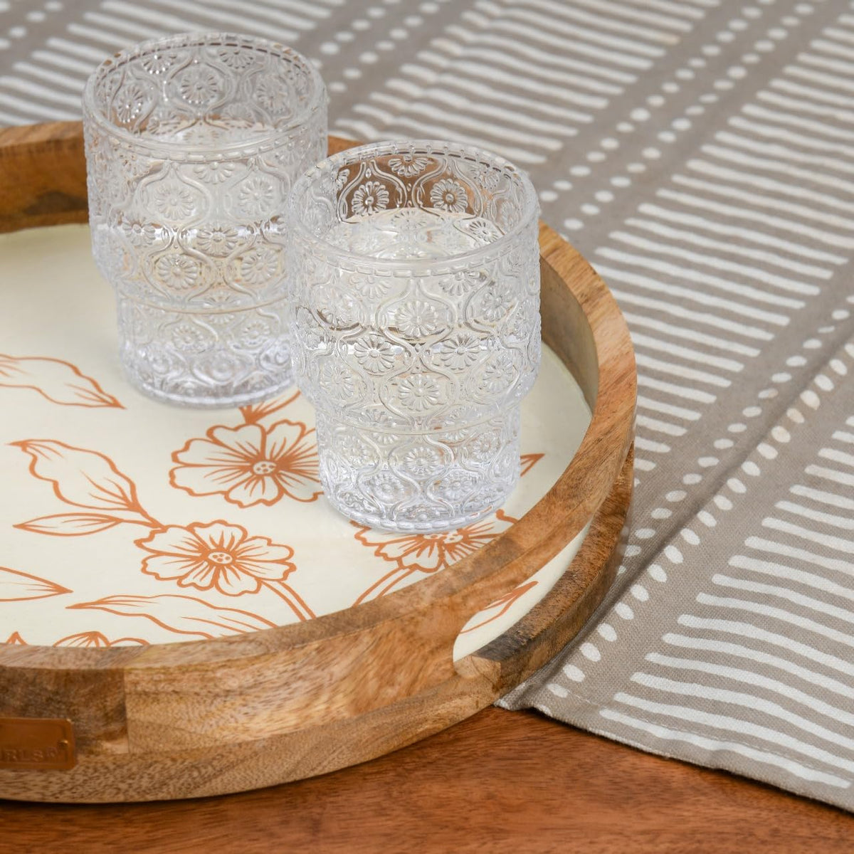 WOOD CURLS round mango wood serving tray with cream base and copper floral design holding two textured glass tumblers