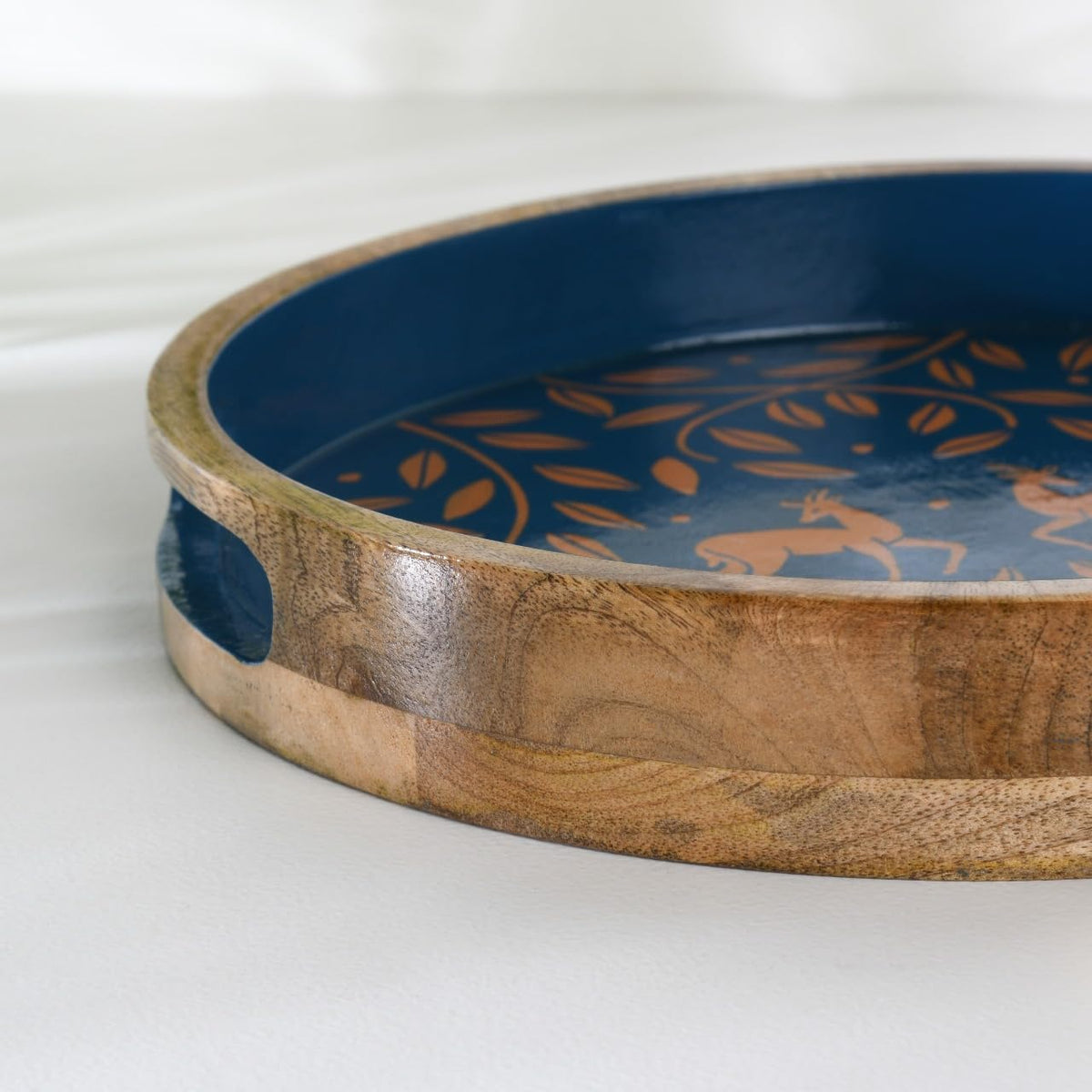 WOOD CURLS round mango wood serving tray with navy blue base, copper antelope and leaf motif, and side handles.