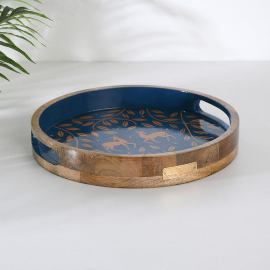 WOOD CURLS round mango wood serving tray with navy blue base, copper antelope and leaf motif, and side handles.