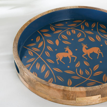 WOOD CURLS round mango wood serving tray with navy blue base, copper antelope and leaf motif, and rustic wood rim.