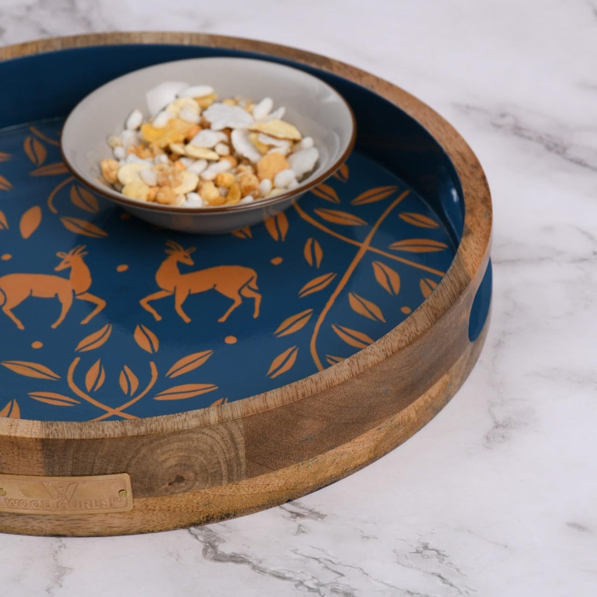 WOOD CURLS round mango wood serving tray with navy blue base, copper antelope and leaf motifs, and a snack bowl.