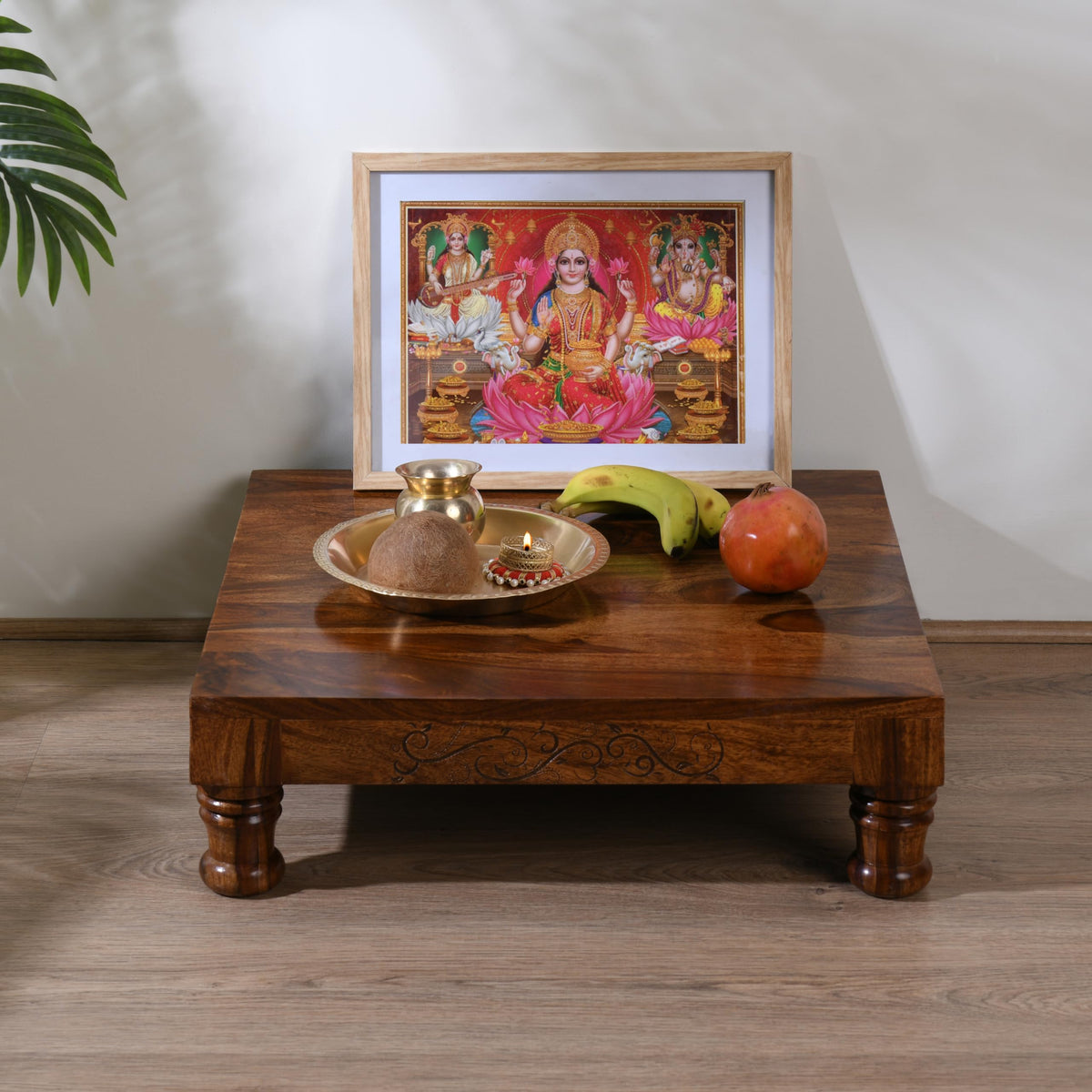 WOOD CURLS Sheesham wood puja chowki with carved legs, holding a brass thali, deity frame, and fruit offerings.