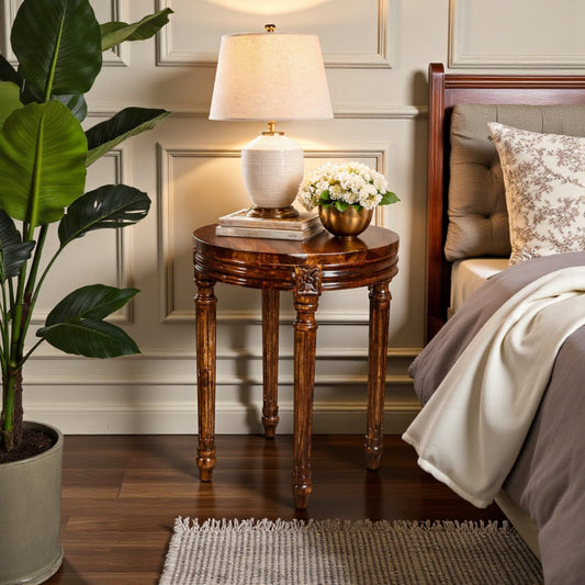 WOOD CURLS round Sheesham wood side table with walnut finish and carved legs, styled as a bedside table with a lamp.
