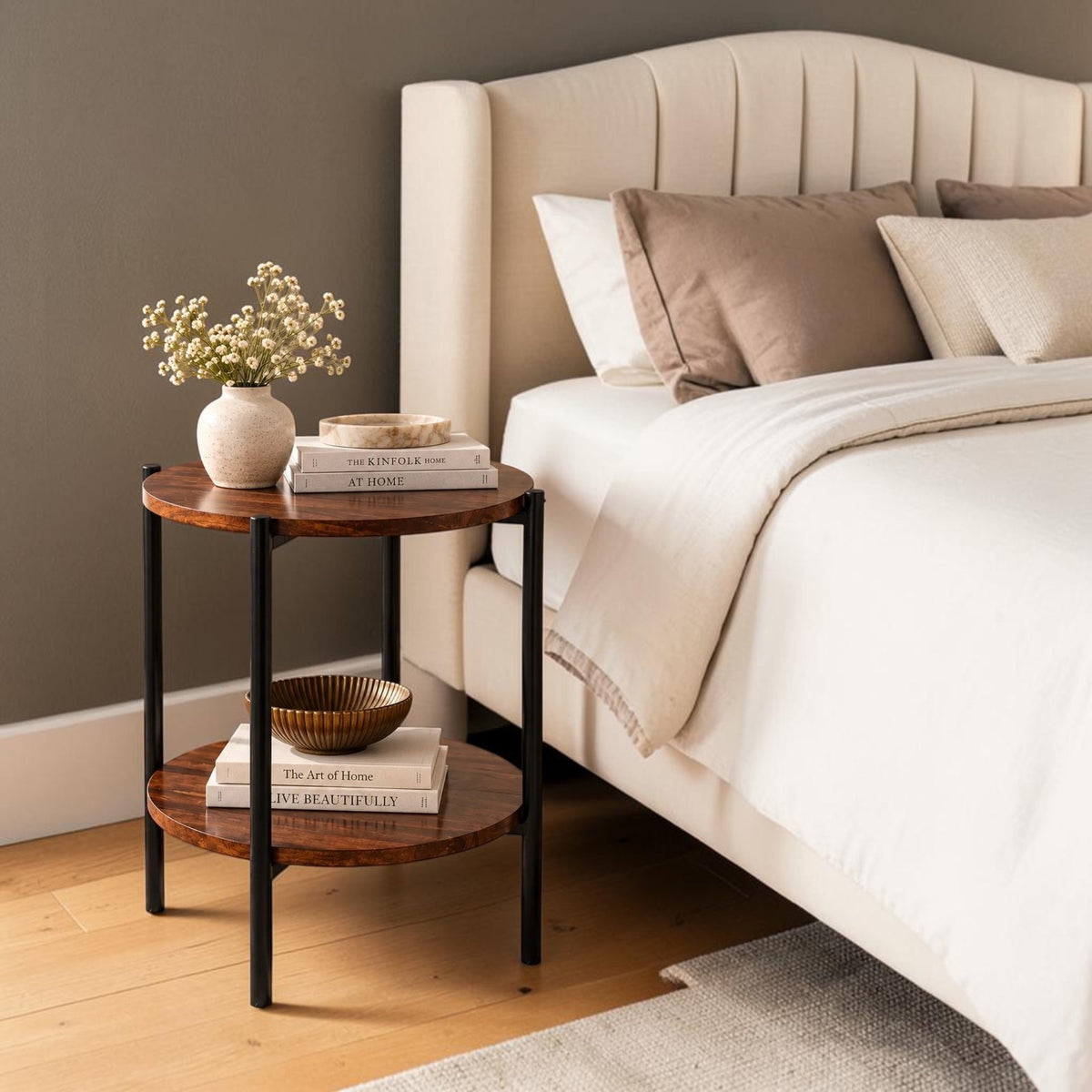 WOOD CURLS round Sheesham wood side table with black metal legs and two shelves beside a beige upholstered bed