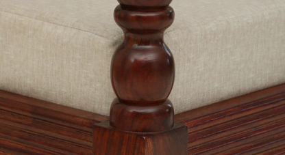 Close-up of WOOD CURLS Auburn three seater sofa featuring carved dark Sheesham wood armrest and beige fabric cushion.