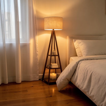 WOOD CURLS walnut mango wood tripod floor lamp with three storage shelves and a fabric shade in a cozy bedroom.