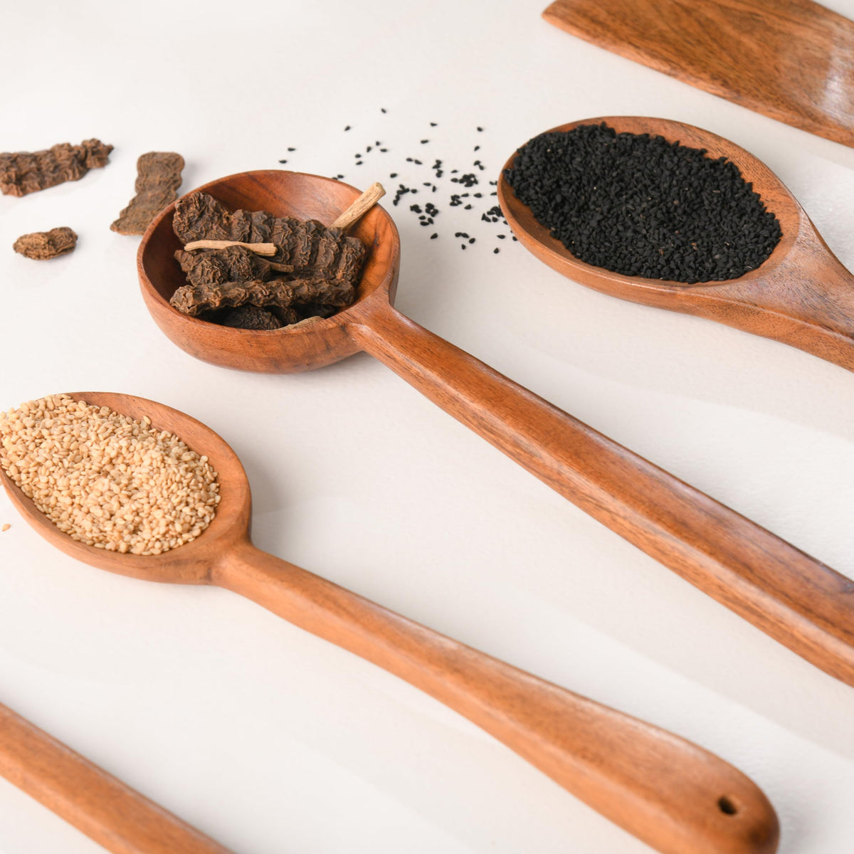 WOOD CURLS wooden kitchen spoons filled with sesame seeds and spices on a white surface