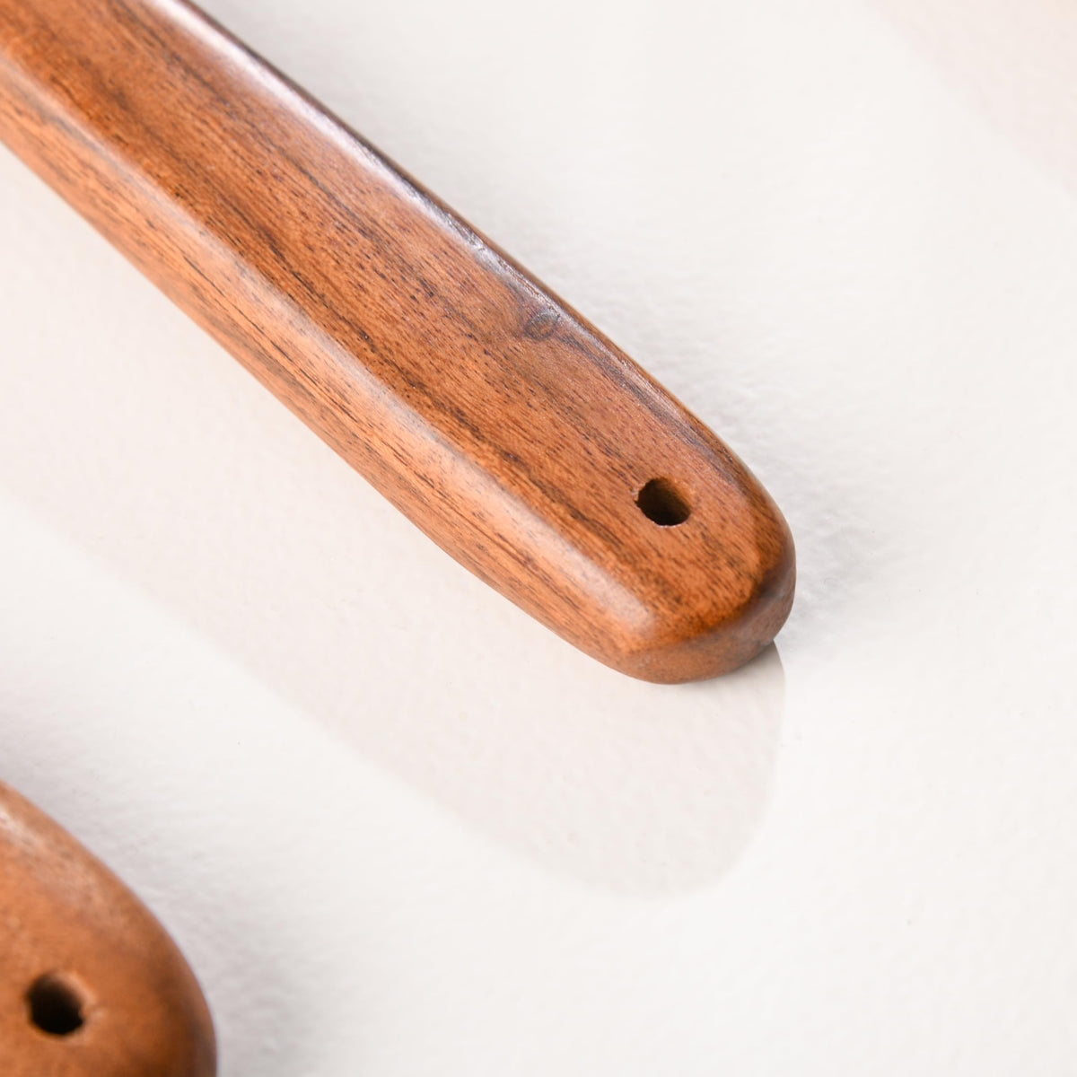 WOOD CURLS wooden kitchen utensil handles with smooth grain and hanging holes on a white surface